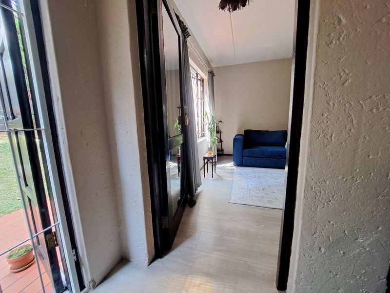 A view through a doorway into a living area featuring light-toned laminate flooring and natural light from large windows.