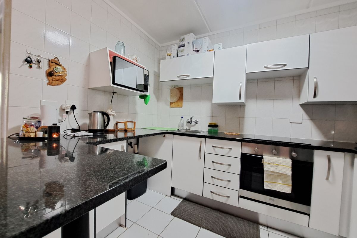 A functional kitchen featuring white cabinetry, dark granite countertops, a built-in oven, and tiled finishes throughout.