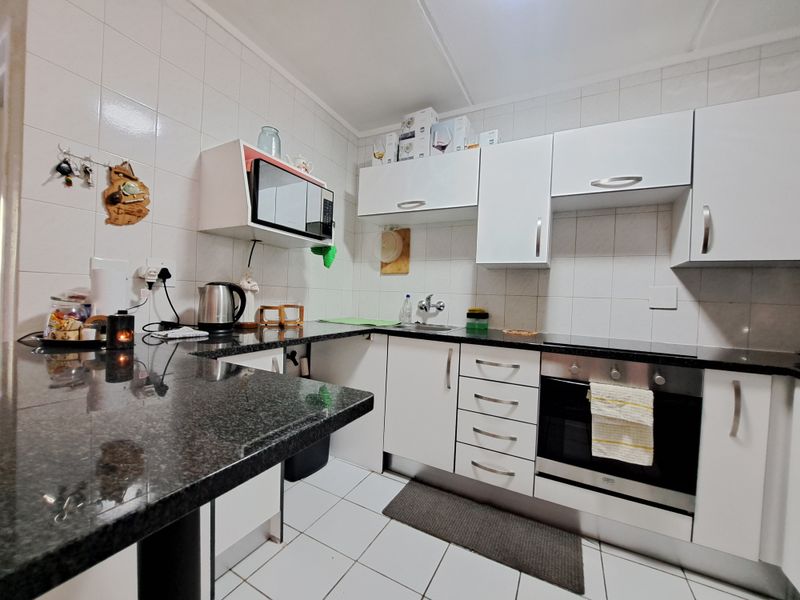 A functional kitchen featuring white cabinetry, dark granite countertops, a built-in oven, and tiled finishes throughout.