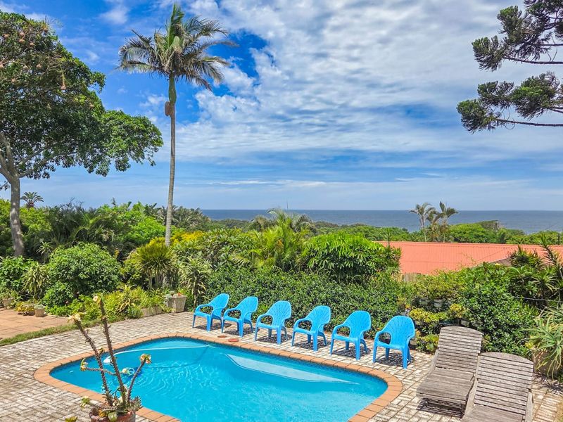 Outdoor pool area featuring a paved deck, established garden surroundings, and scenic ocean views.