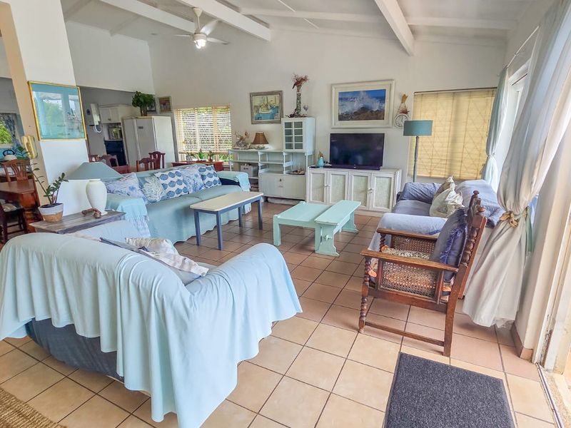 Spacious open-plan living area featuring tiled floors, exposed beam ceilings, and large sliding doors providing seamless access to the outdoor patio space.