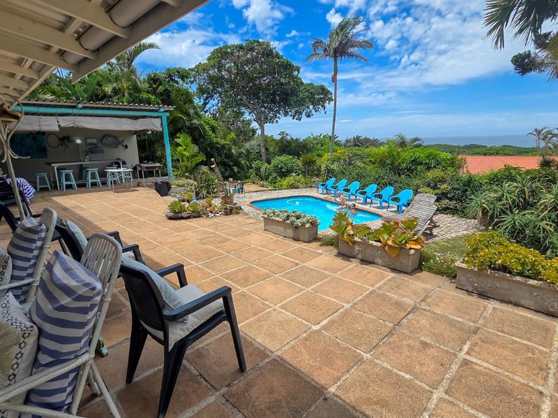 Spacious outdoor entertainment area featuring a paved patio, covered veranda, swimming pool, and scenic coastal views.