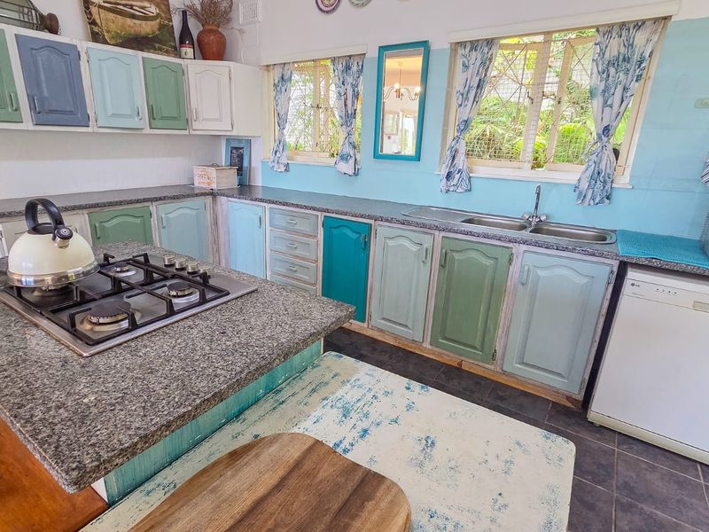 A functional kitchen featuring granite countertops, a gas hob, double basin sink, and ample built-in cabinetry with a unique multi-colored finish.
