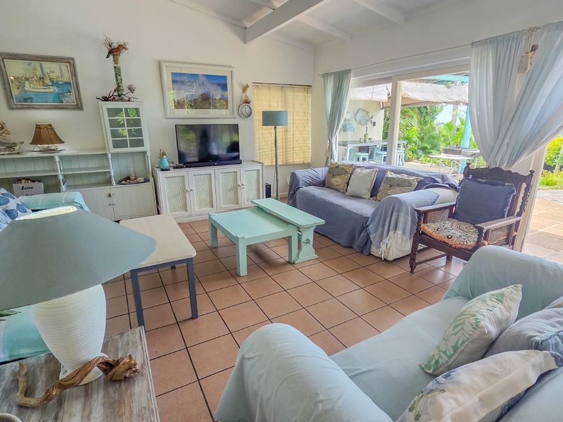 A bright living room featuring tiled floors, exposed beam ceilings, and large sliding glass doors that open onto a patio and pool area.