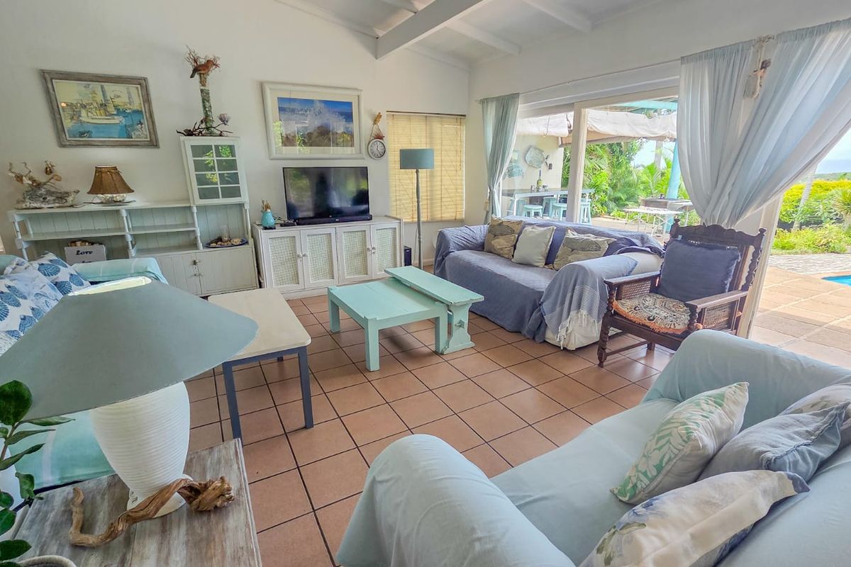 A bright living room featuring tiled floors, exposed beam ceilings, and large sliding glass doors that open onto a patio and pool area.