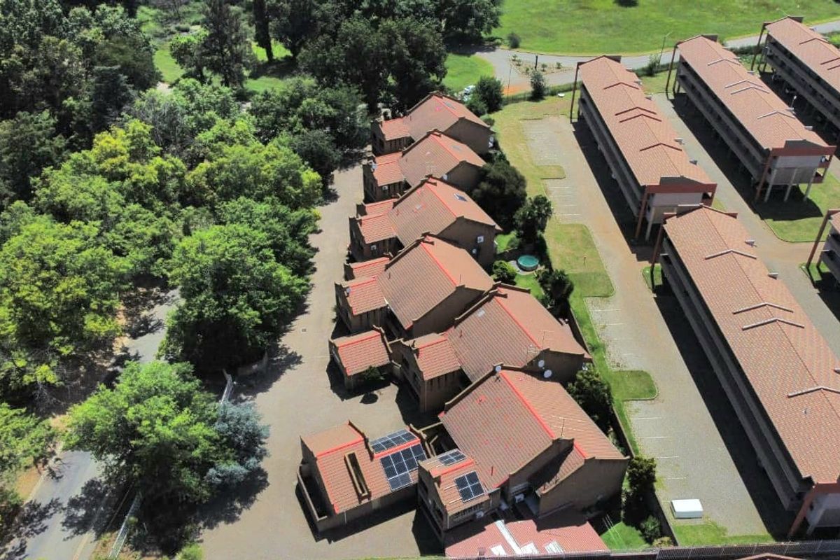Aerial view of the townhouse complex featuring multiple residential units with tiled roofs, solar panels, and surrounding landscaped grounds.