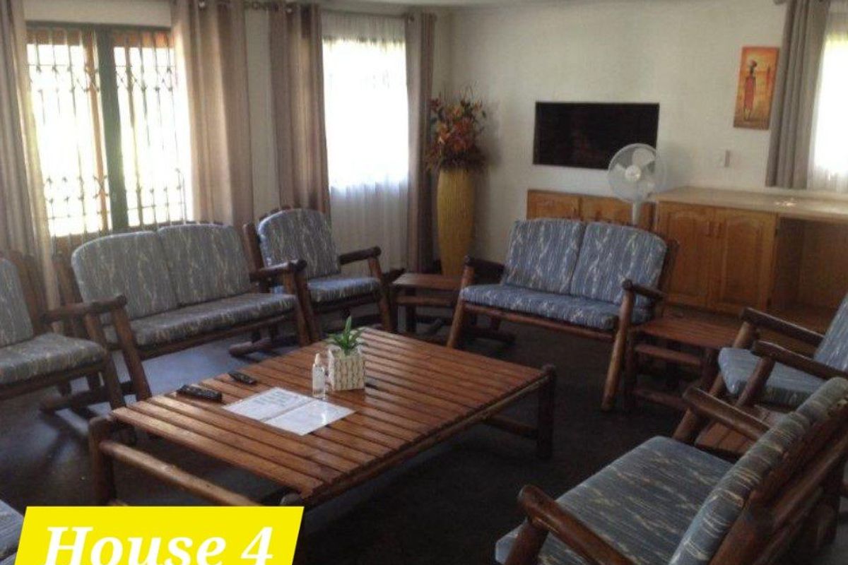 A spacious living room featuring tiled flooring, large windows with security gates, and built-in wooden cabinetry.