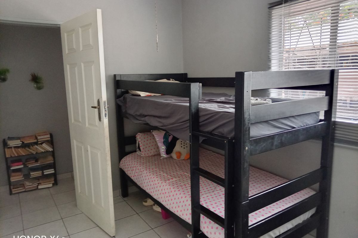 A bedroom featuring tiled flooring and horizontal window blinds, providing a functional space for sleeping.