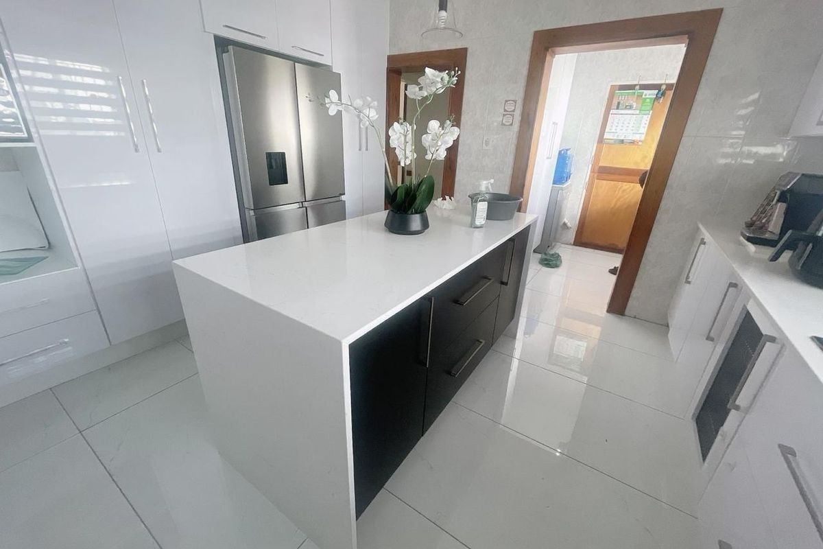 Modern kitchen featuring a central island with stone countertop, high-gloss cabinetry, and polished floor tiles, leading into an adjacent utility area.