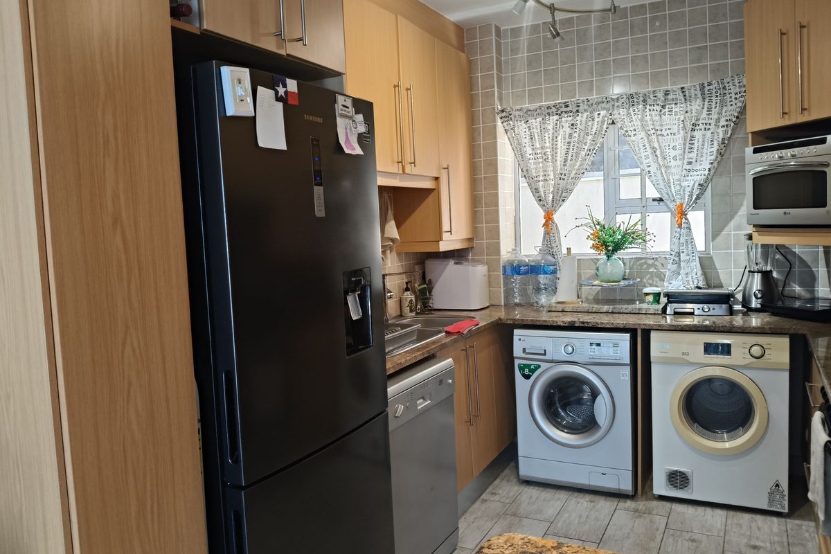 A functional kitchen featuring light wood cabinetry, granite countertops, tiled backsplash, and integrated laundry appliances including a washing machine and tumble dryer.