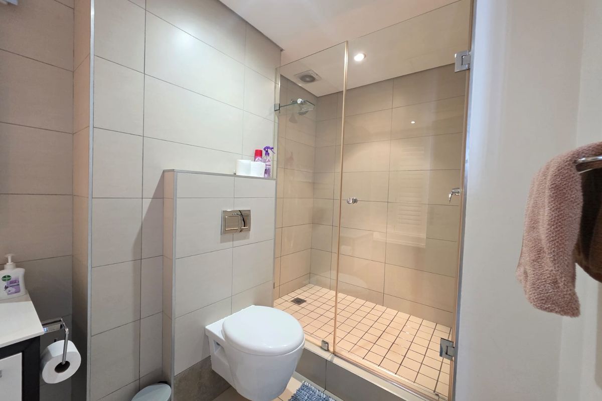 Modern bathroom featuring a wall-mounted toilet, a glass-enclosed walk-in shower with tiled flooring, and neutral wall tiling throughout.