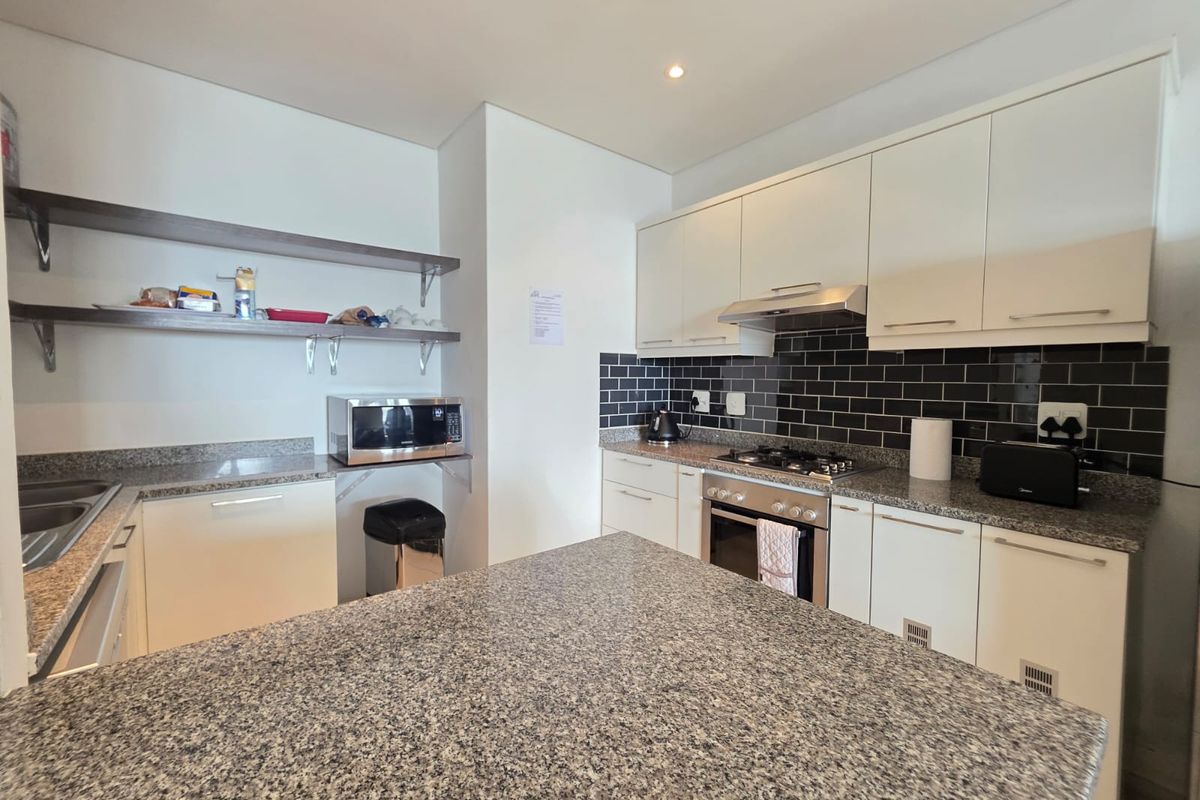Modern kitchen featuring white cabinetry, granite countertops, a central island, and a stylish black subway tile backsplash with integrated stainless steel appliances.