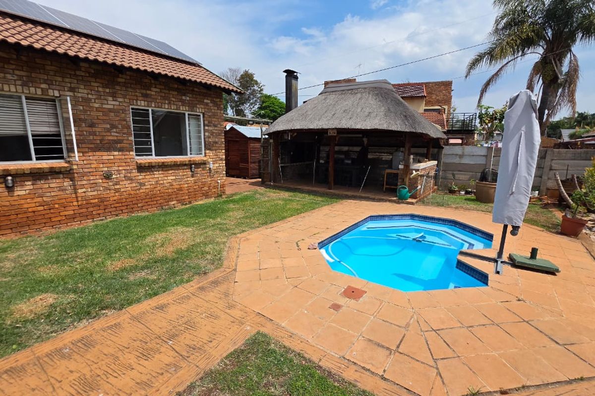 Rear garden featuring a swimming pool, paved surround, and a thatched lapa entertainment area adjacent to the brick-built house.
