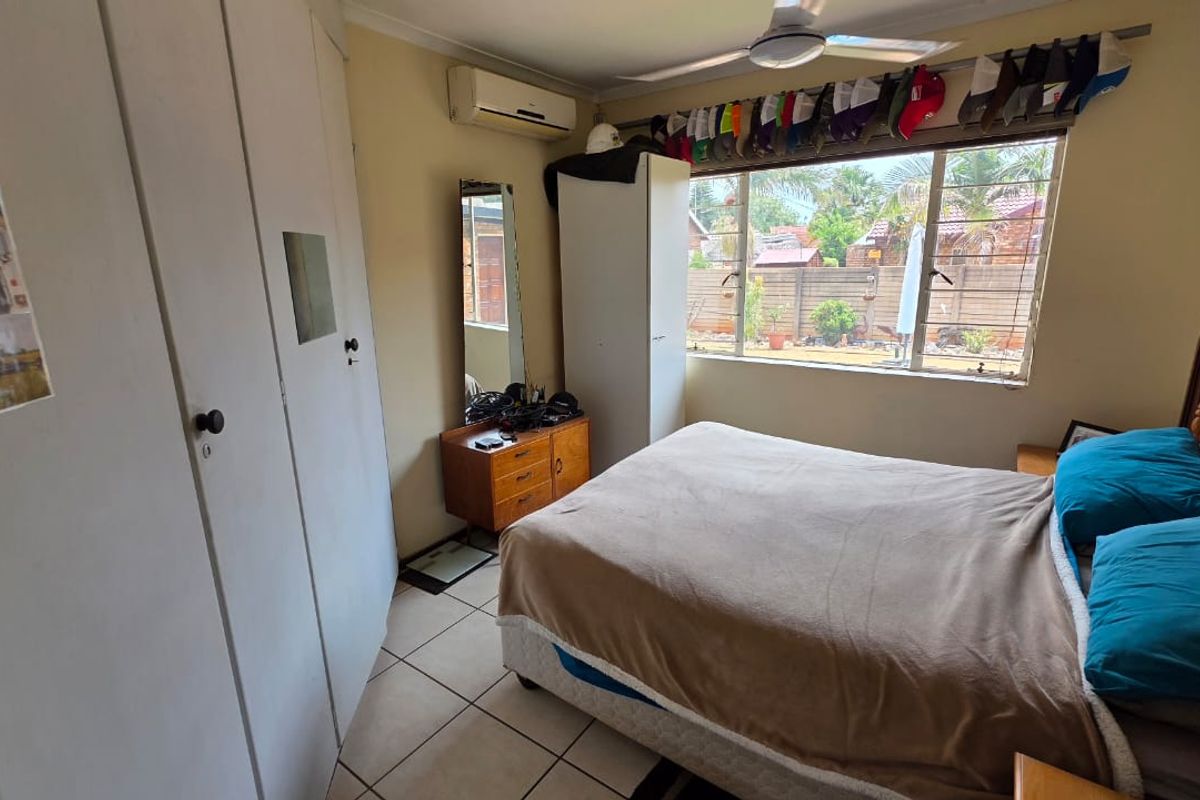 A functional bedroom featuring built-in cupboards, tiled flooring, a ceiling fan, and a wall-mounted air conditioning unit.