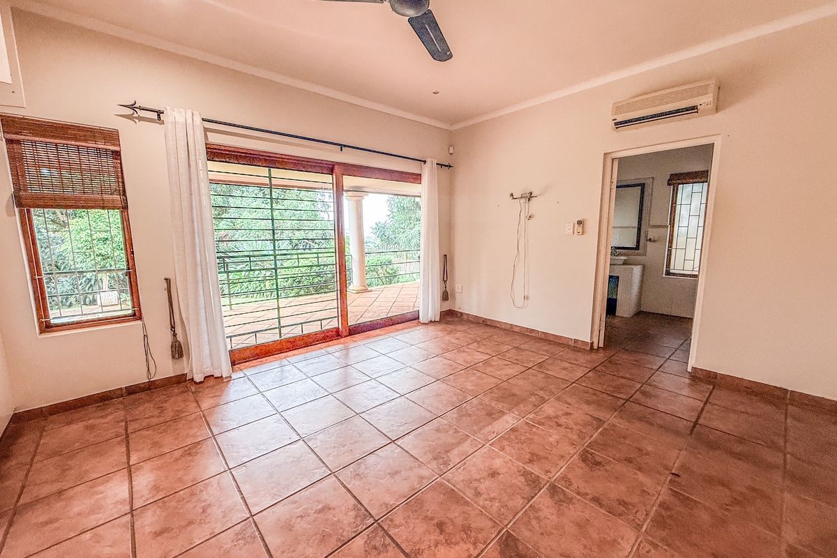 Spacious living area featuring terracotta floor tiles, a ceiling fan, wall-mounted air conditioning unit, and sliding glass doors leading to an outdoor patio.