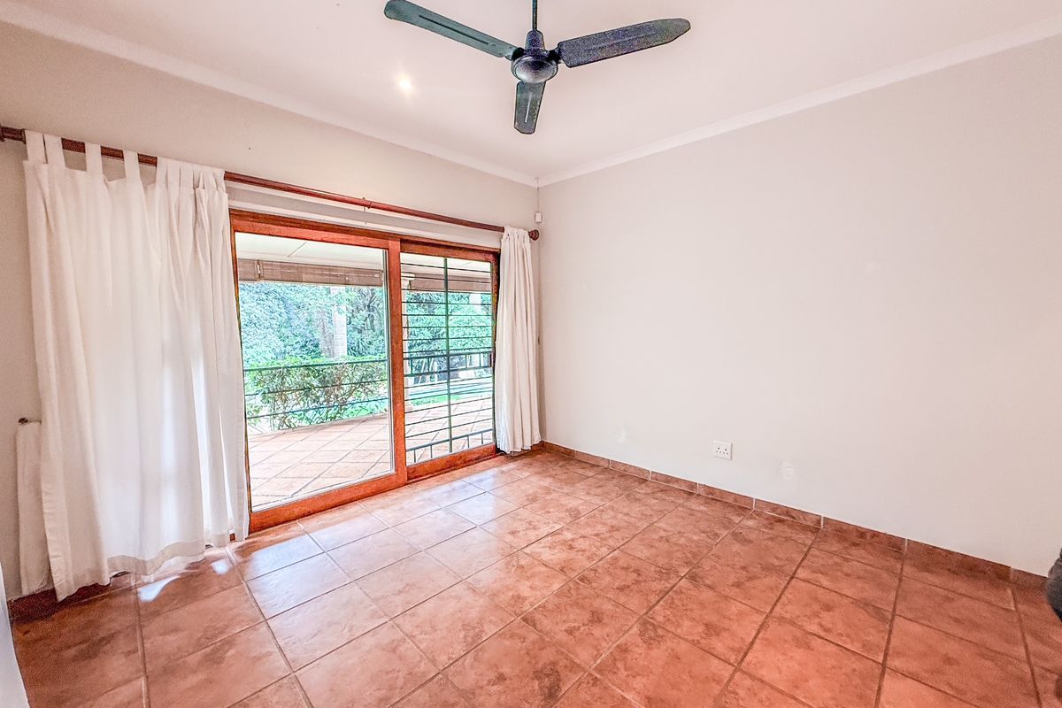 A bright, empty bedroom featuring terracotta floor tiles, a ceiling fan, and sliding glass doors that open onto an outdoor patio area.