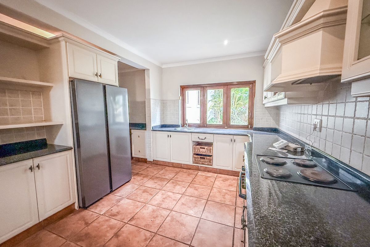 A functional kitchen featuring granite countertops, built-in cabinetry, a ceramic hob, and tiled flooring with a window overlooking the garden.