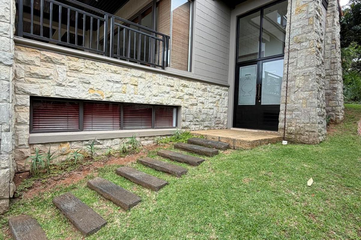 Exterior view of the townhouse featuring stone cladding, a covered balcony with black railings, and a paved walkway leading to the entrance.