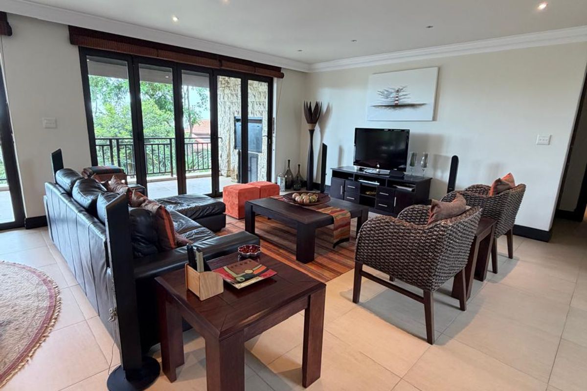Spacious living room featuring large sliding glass doors leading to a balcony, recessed ceiling lighting, and neutral floor tiling throughout.
