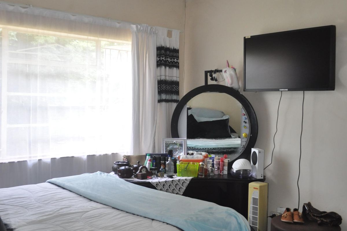 A bedroom featuring a ceiling fan, large window with security bars, and wall-mounted television point.
