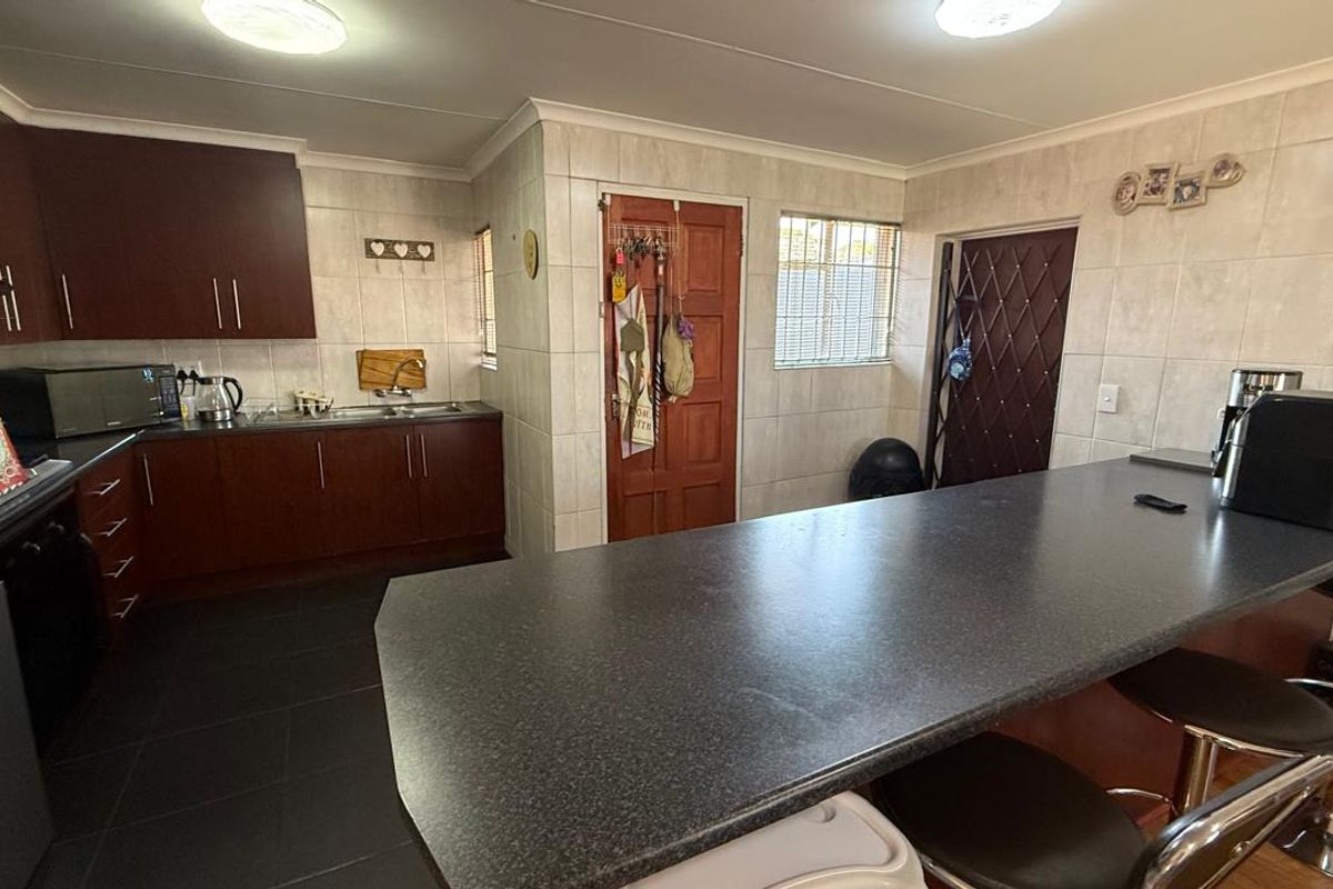 A functional kitchen featuring dark wood cabinetry, a large breakfast bar with stone-look countertop, and tiled walls and flooring.
