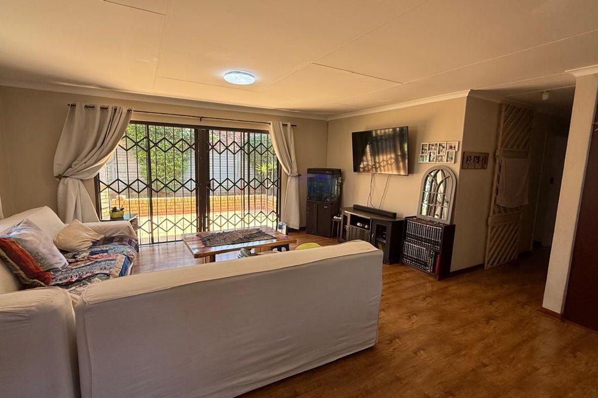 A comfortable living room featuring wood-look flooring, a ceiling-mounted light fixture, and sliding glass doors with security gates leading to the outdoor area.
