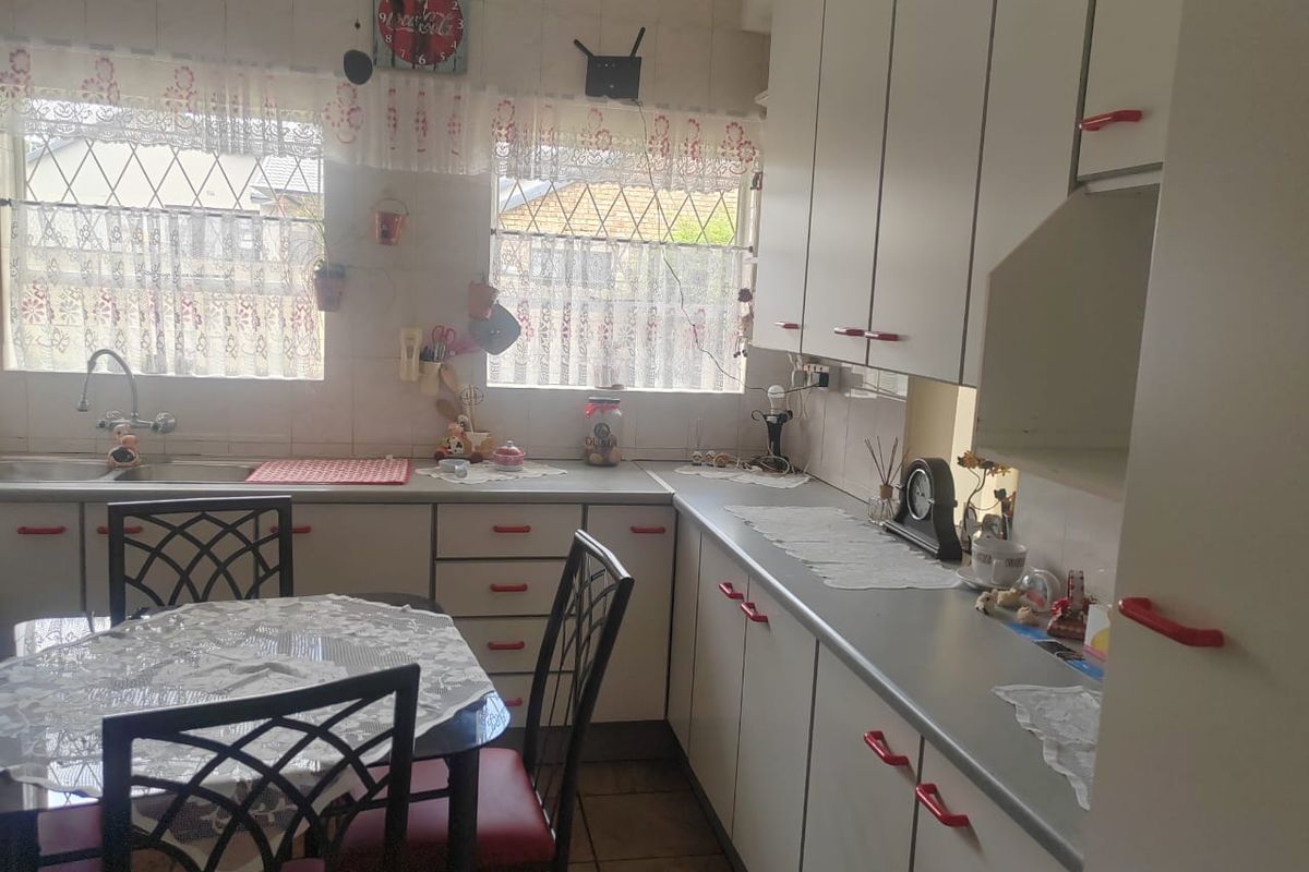 A functional kitchen featuring white cabinetry with red handles, tiled splashbacks, and a dedicated breakfast nook area.