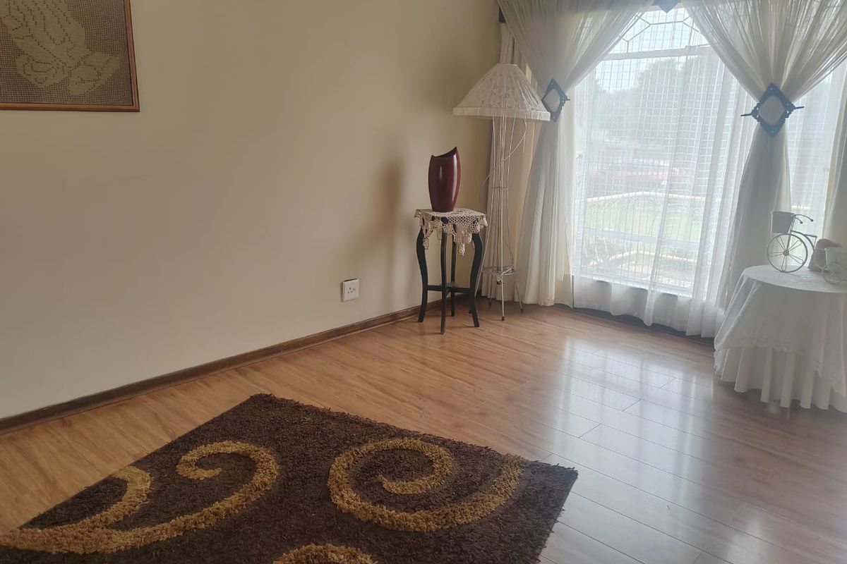 A bright living room featuring light wood-look laminate flooring and large windows with sheer curtains, providing ample natural light.