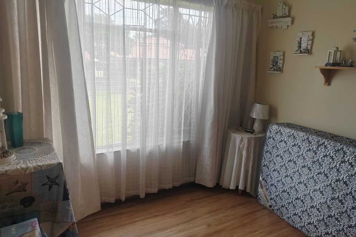 A bedroom featuring laminate flooring and a large window with security bars, providing natural light and a view of the garden.