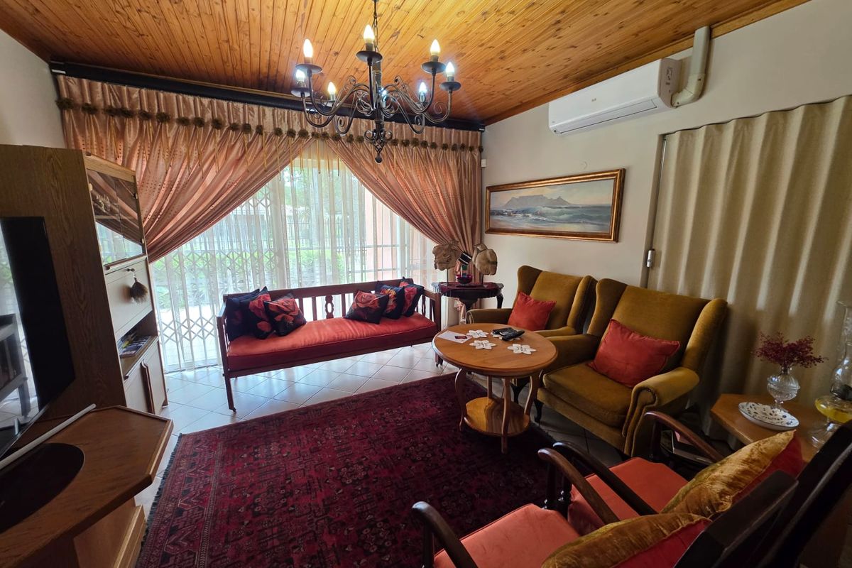 A cozy living room featuring a timber-clad ceiling, tiled flooring, and a wall-mounted air conditioning unit, with large sliding doors leading to the exterior.