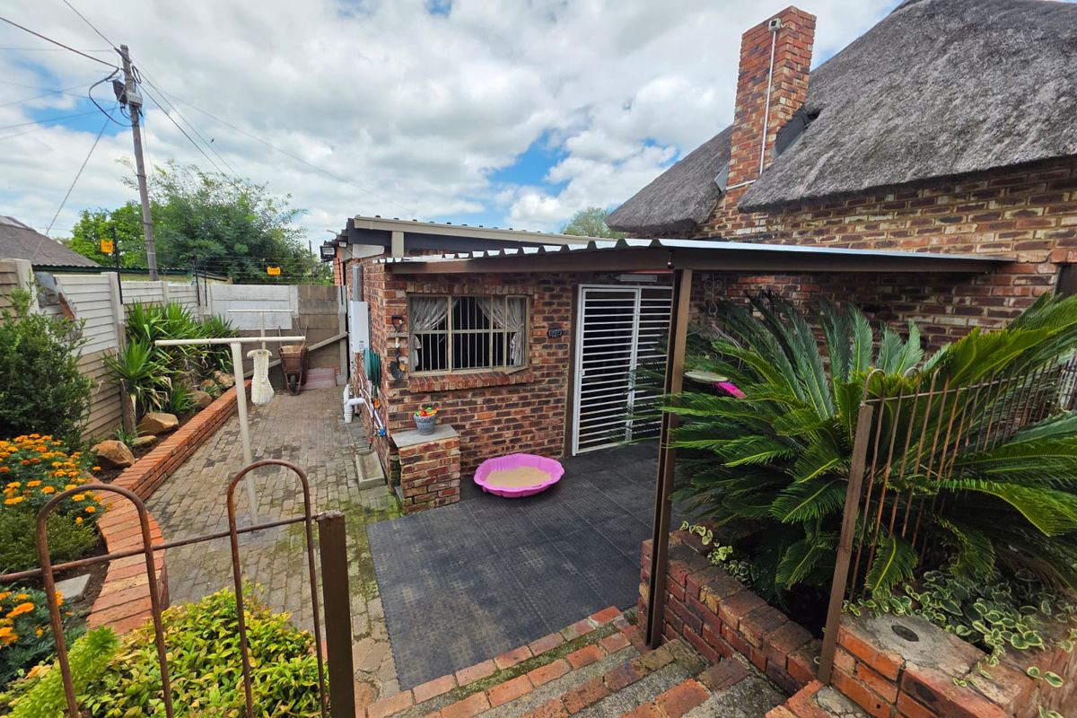 Rear exterior view featuring a thatched roof house, brick facade, and a covered patio area with paved garden surroundings.