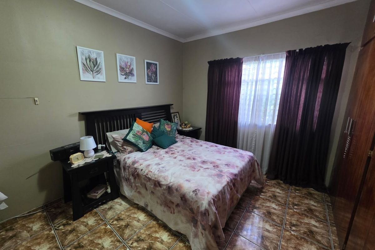 A functional bedroom featuring tiled flooring, a built-in wardrobe, and natural light through a window with curtain rails.