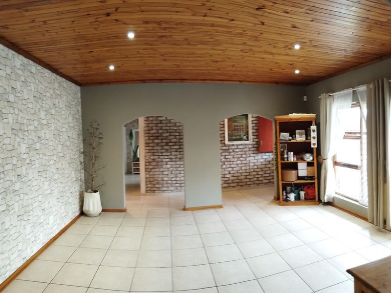 Spacious living area featuring a warm timber tongue and groove ceiling, tiled flooring, and distinctive arched doorways leading to adjacent rooms.