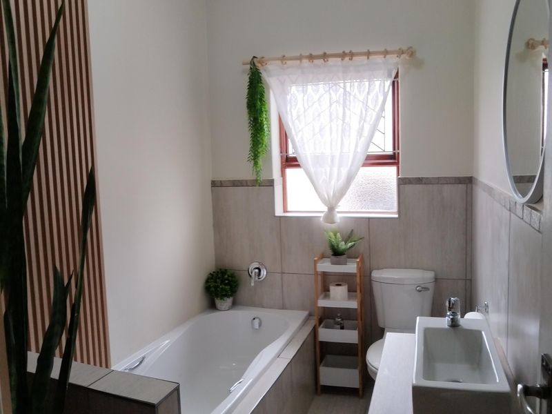 A modern bathroom featuring a built-in bathtub, a vessel sink vanity, and a stylish slatted wood accent wall with neutral tiling.