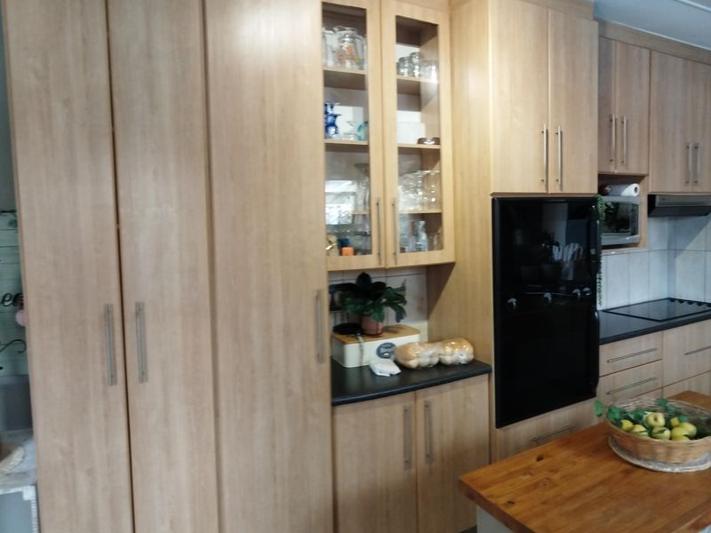 A functional kitchen featuring light wood-toned cabinetry, integrated appliances including an oven and microwave, and ample storage space with glass-fronted display units.