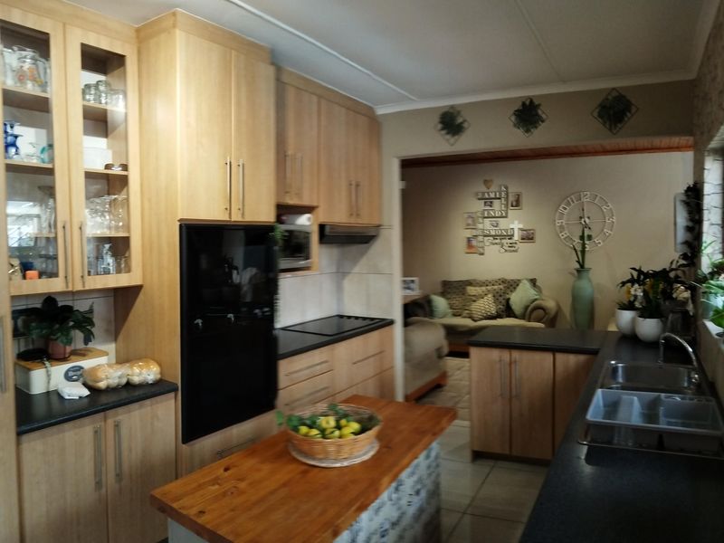 A functional kitchen featuring light wood cabinetry, dark countertops, a central island, and integrated appliances, with an open-plan flow into the adjacent living area.