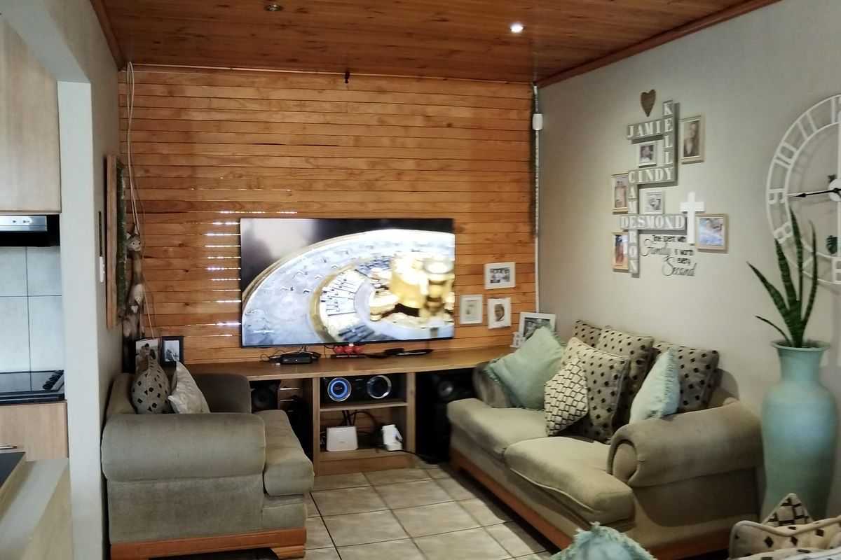 A cozy living room featuring a warm timber-clad ceiling and matching feature wall, complemented by neutral ceramic floor tiles and recessed lighting.