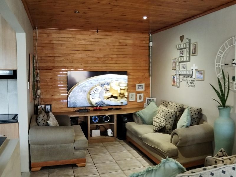 A cozy living room featuring a warm timber-clad ceiling and matching feature wall, complemented by neutral ceramic floor tiles and recessed lighting.