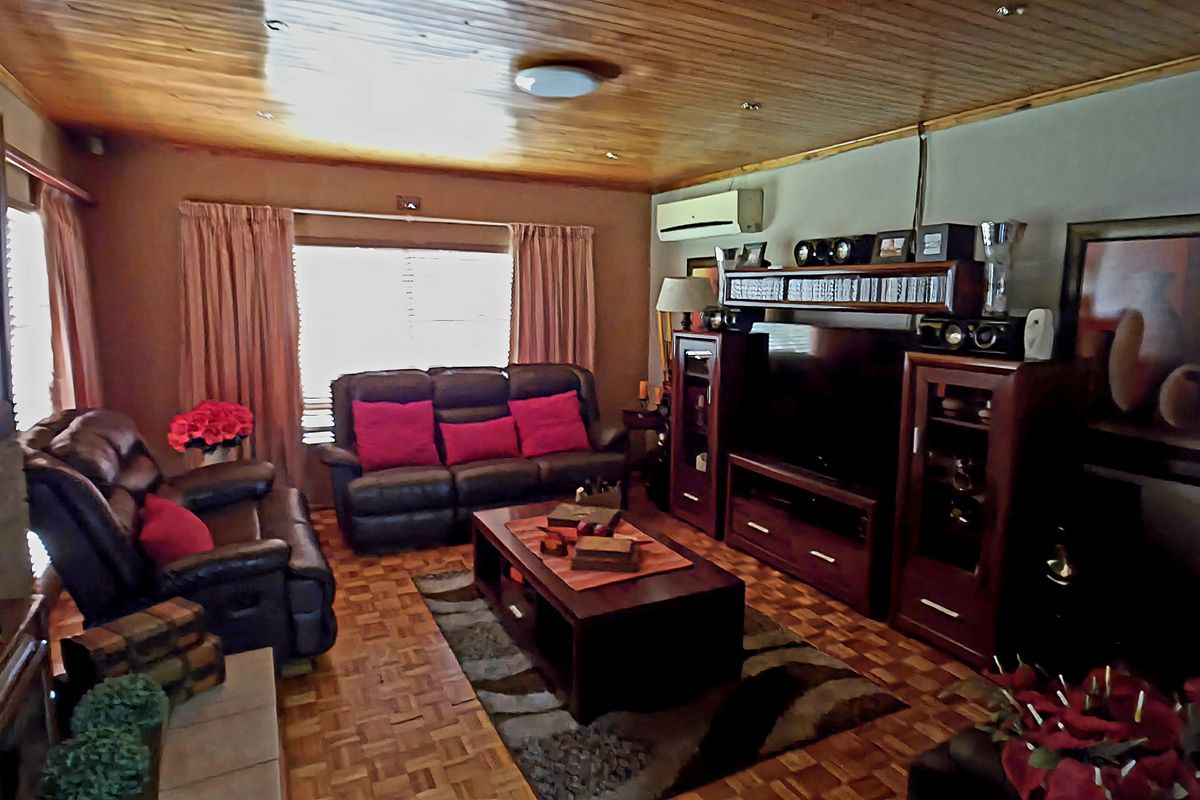 A cozy living room featuring warm timber ceilings, classic parquet flooring, and a brick fireplace, creating a comfortable and inviting atmosphere.