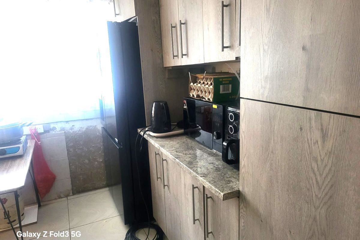 A kitchen area featuring wood-look cabinetry, granite-style countertops, and tiled flooring, currently showing signs of unfinished wall surfaces near the window.