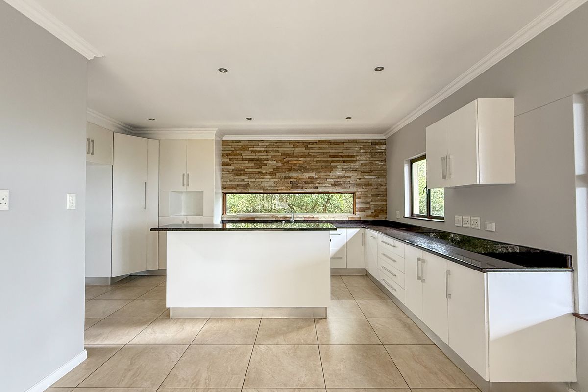 Modern kitchen featuring white cabinetry, dark granite countertops, a central island, and a decorative stone feature wall with a horizontal window.