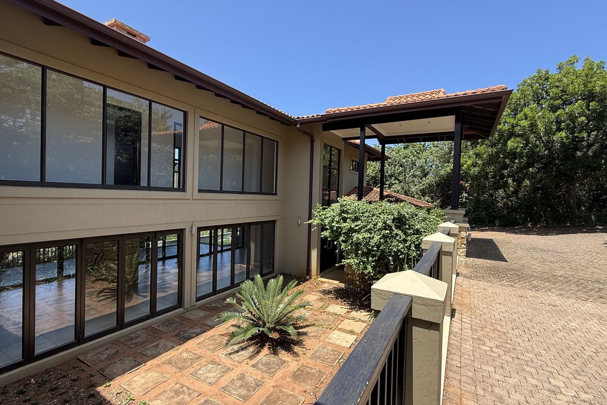 A view of the rear exterior facade featuring large glass windows, a covered patio area, and paved driveway access.