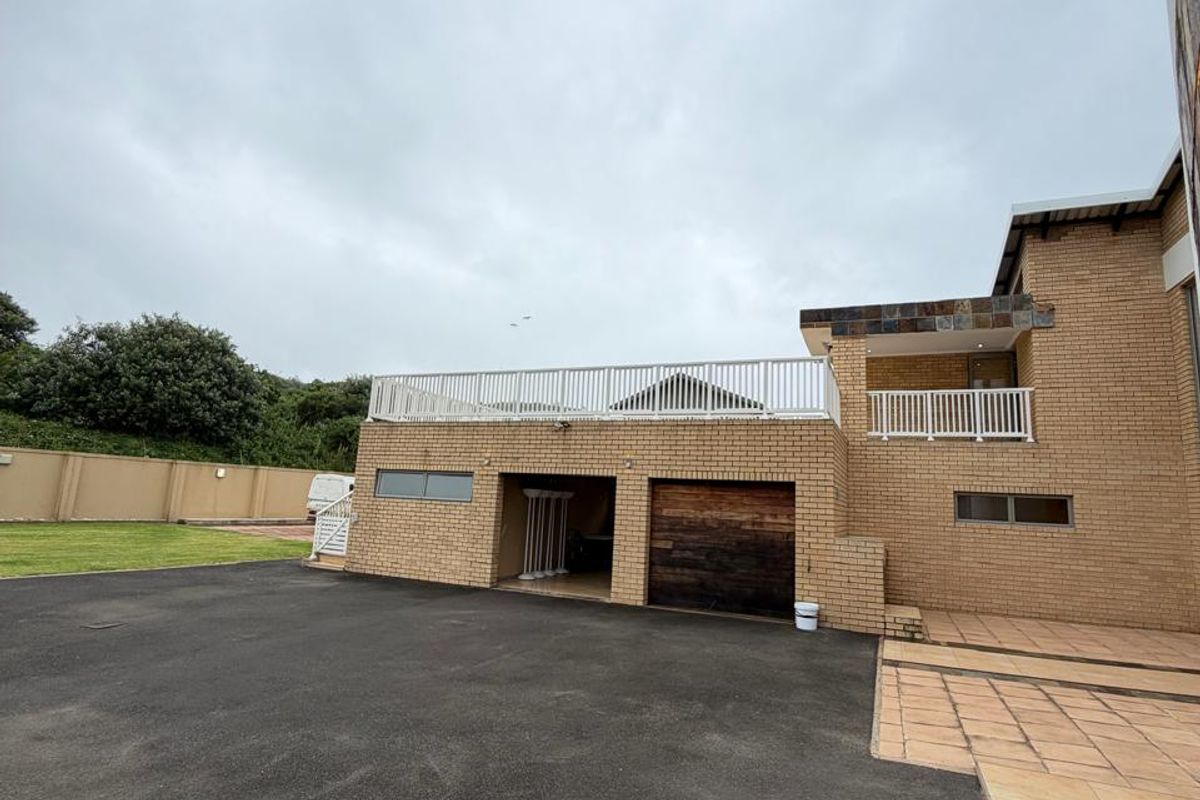 Rear exterior view featuring a brick facade, asphalt driveway, tiled patio area, and an upper-level balcony with white railings.