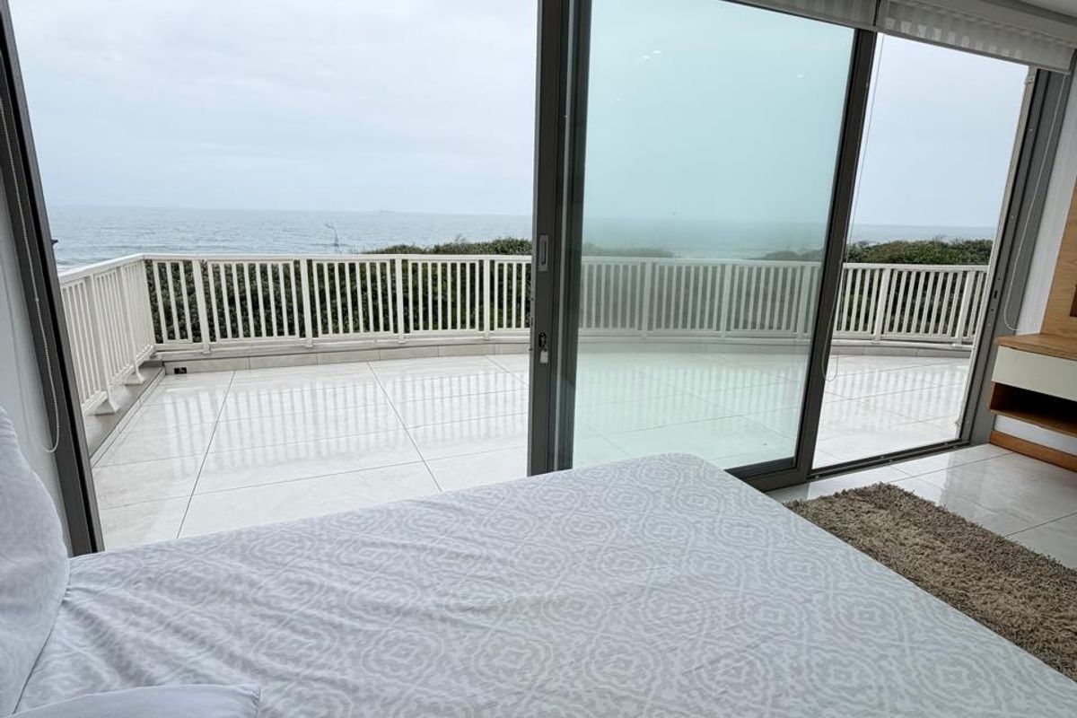 A modern bedroom featuring large sliding glass doors that open onto a private balcony with expansive ocean views and tiled flooring.