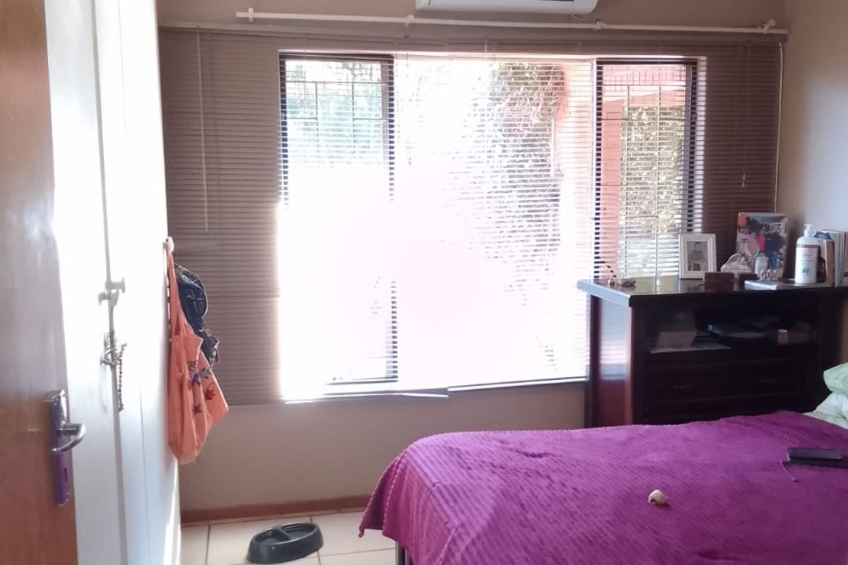 A bedroom featuring tiled flooring, built-in cupboards, a ceiling fan, and a wall-mounted air conditioning unit.