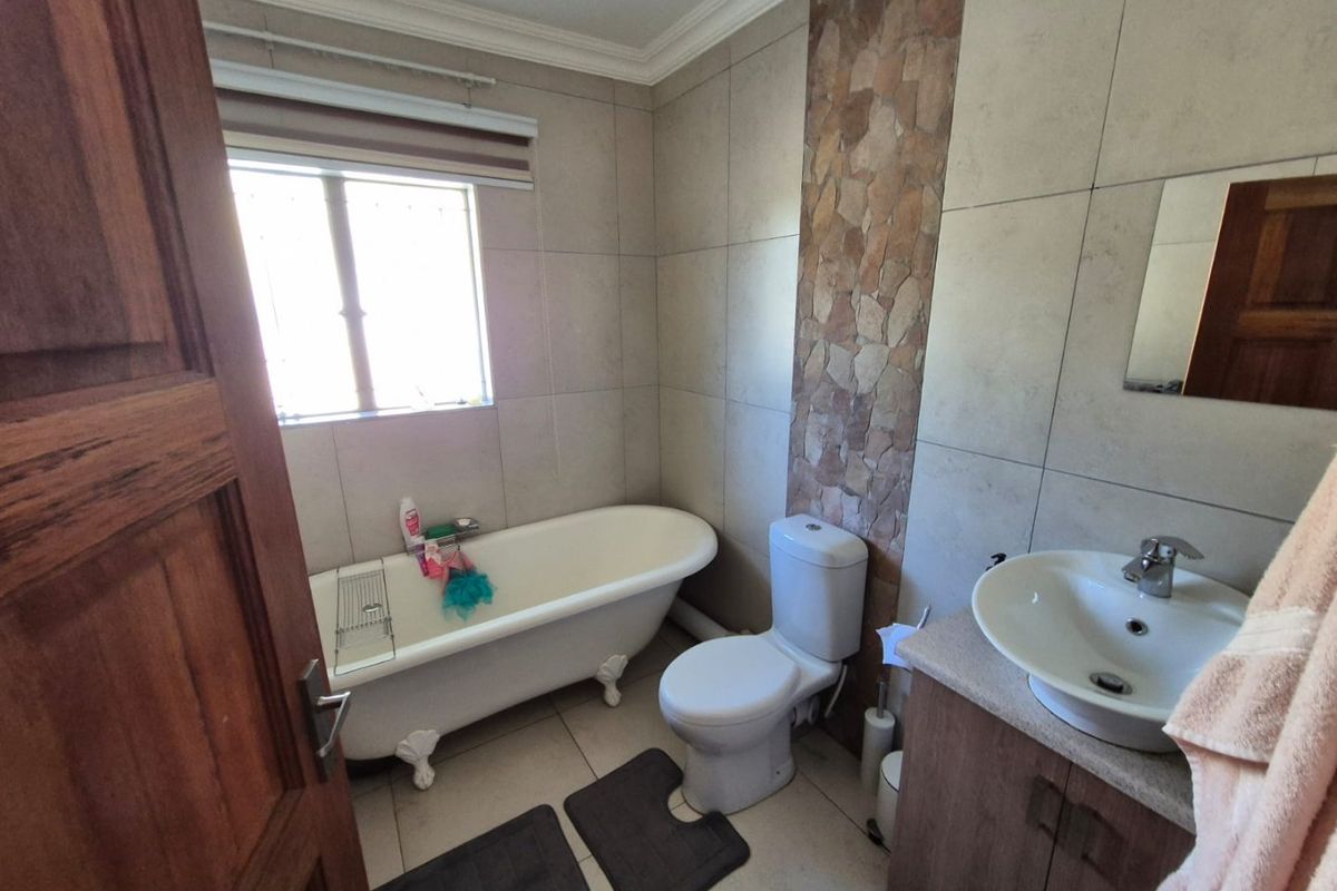 A functional bathroom featuring a classic clawfoot bathtub, a pedestal-style vanity with a vessel sink, and decorative stone-cladding wall accents.