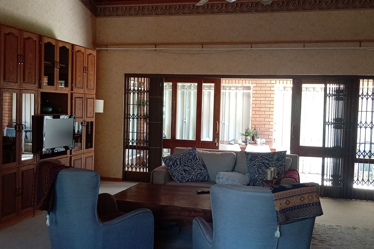 Spacious living room featuring built-in wooden cabinetry, high ceilings with decorative cornicing, and large sliding doors leading to an outdoor patio area.