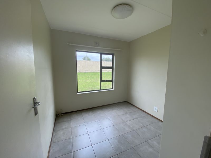 A bright, empty bedroom featuring neutral wall paint, tiled flooring, and a large window overlooking the garden area.