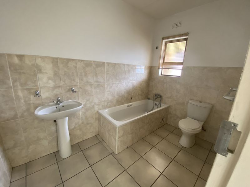 A functional bathroom featuring a pedestal basin, built-in bathtub, and toilet, finished with neutral ceramic wall and floor tiles.