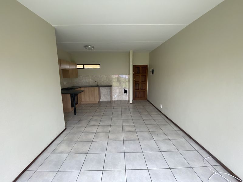 An open-plan living and kitchen area featuring tiled flooring, built-in cabinetry, and a functional kitchen layout in a vacant townhouse setting.